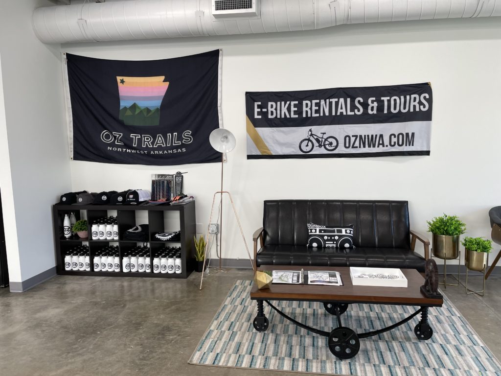OZ E-Bikes waiting area with seating, a table and a shelf full of bottles and accessories.